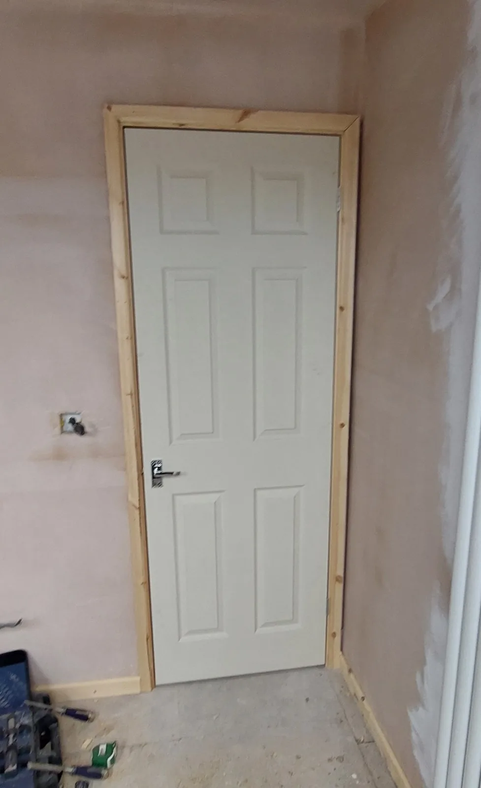 Internal door newly fitted in a freshly plastered hallway, with toolbox and tools on the floor mid-job.