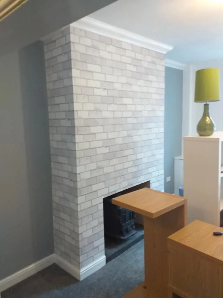 Whitewashed feature brick chimney breast in a living room, framed by grey walls with a wood-burning stove inset at the base.